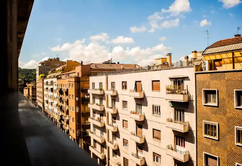 Sunny urban balcony view showing neighboring apartment facades and a blue sky — ideal for listings highlighting a city-facing terrace or balcony.