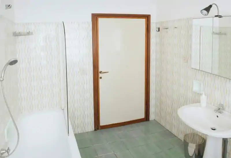 Bagno luminoso e ben inquadrato con vasca, doccia a mano, lavabo e specchio — arredi semplici e piastrelle a motivo.