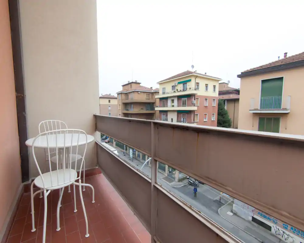 Petit balcon urbain avec une table ronde blanche et deux chaises assorties, donnant sur une rue calme et des immeubles voisins — idéal pour le café du matin.