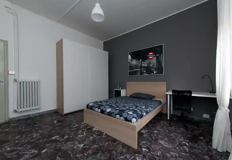 Dormitorio moderno y luminoso con cama individual, armario y escritorio junto a la ventana. Tonos neutros y una foto en blanco y negro aportan un ambiente elegante y relajado, perfecto para una estancia cómoda.