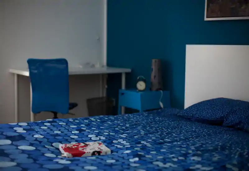 Chambre lumineuse et stylée avec une couette bleue à motifs, table de chevet et bureau en arrière-plan — chaleureuse et bien composée pour une annonce.