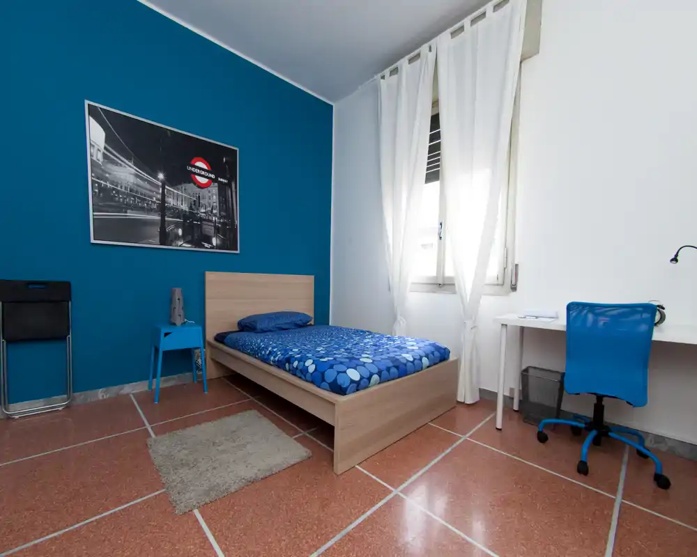 Chambre simple lumineuse et moderne avec un lit en bois, un mur bleu contrastant et une literie assortie. Une fenêtre apporte la lumière naturelle et un petit bureau crée un coin étude pratique.