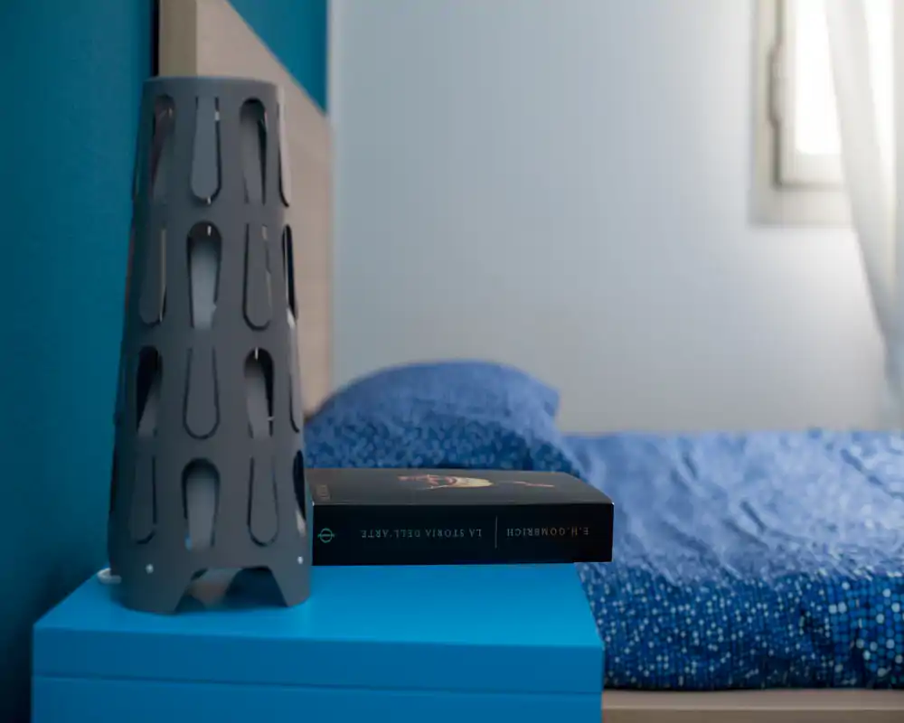 Coin de chambre moderne et lumineux avec une couette bleue à motifs, une table de chevet et une lampe décorative près d'une fenêtre lumineuse.