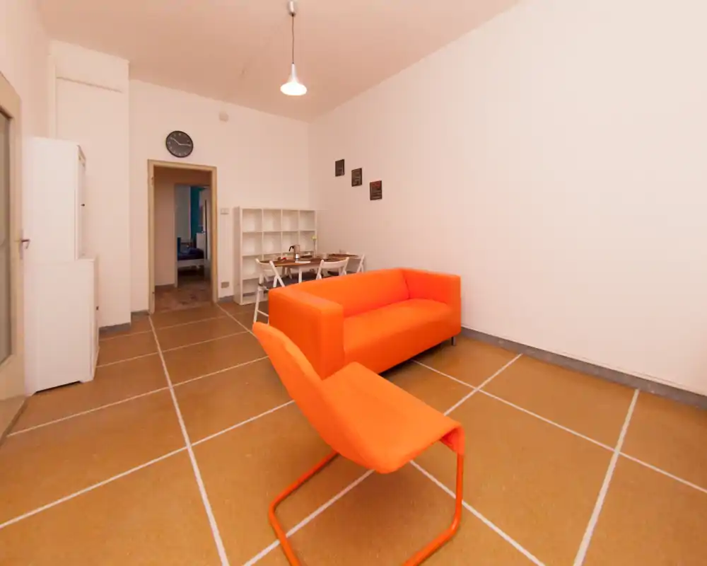 Espace de vie lumineux et moderne avec canapé orange vif et fauteuil assorti, décor minimaliste et petite table à manger/bureau à l'arrière.