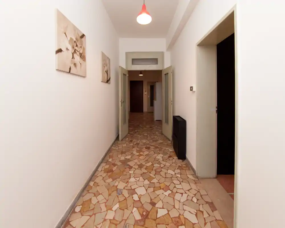 Long couloir d'entrée bien éclairé avec sol carrelé décoratif, murs blancs et lampe au plafond ; portes doubles donnant sur les pièces intérieures.