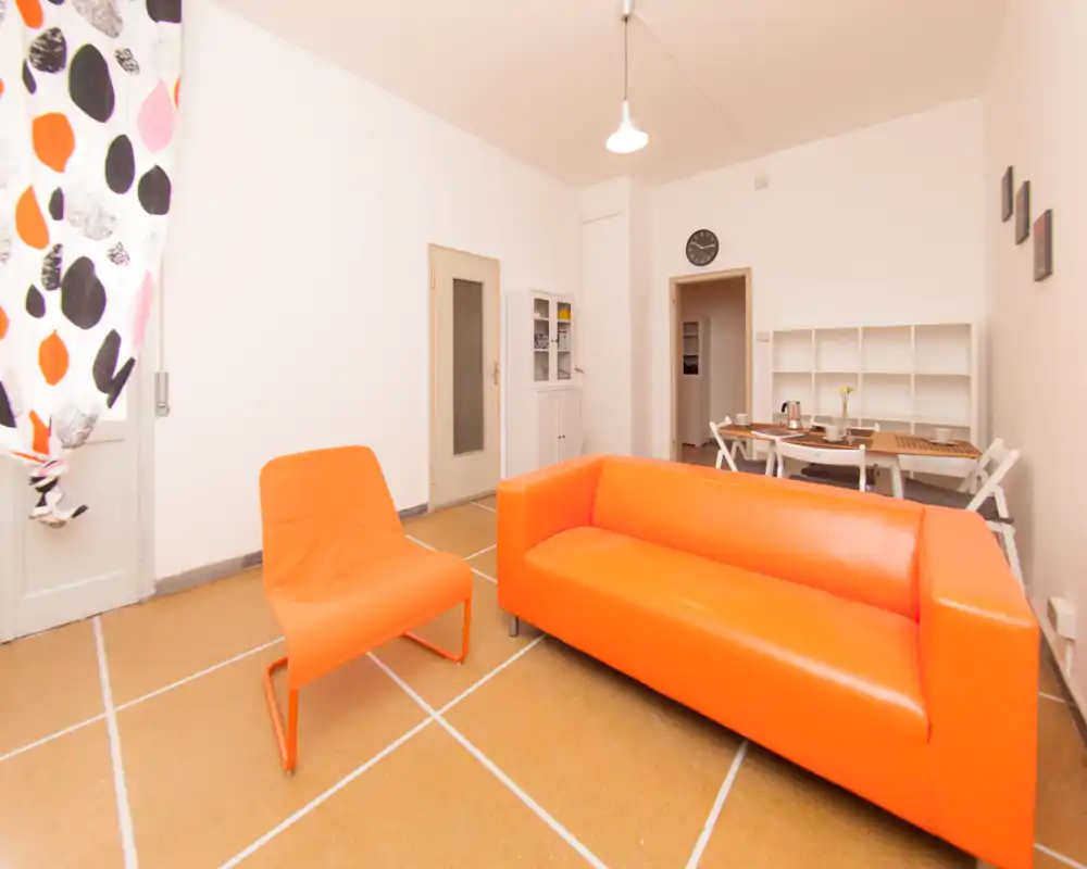Salon lumineux et moderne avec un canapé orange vif et un fauteuil assorti, coin repas simple et étagères blanches épurées — parfait pour des locations courtes au style dynamique.
