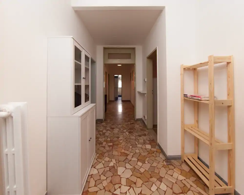 Entrée/couloir lumineux avec sol en terrazzo à motifs, meuble blanc et étagères ouvertes — un couloir d’entrée propre et fonctionnel offrant une vue sur les pièces adjacentes.