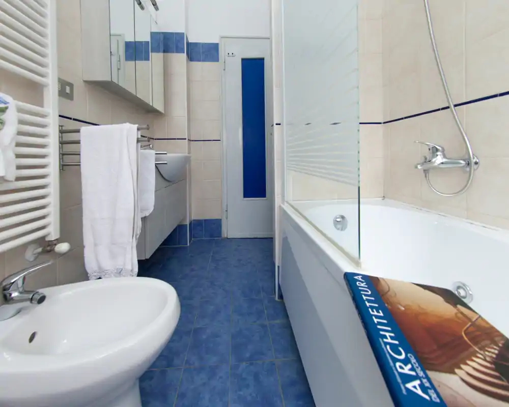 Salle de bains moderne et propre avec carrelage bleu au sol, baignoire avec paroi en verre, bidet et lavabo mural avec armoires-miroirs.