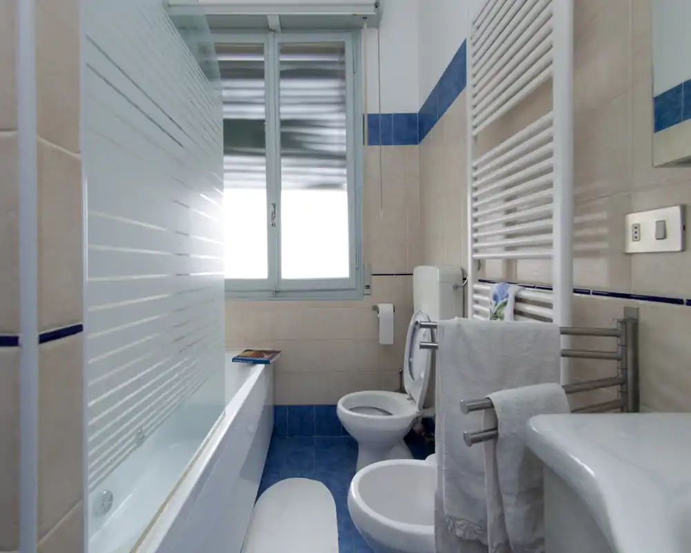 Salle de bains lumineuse et soignée avec baignoire, WC, bidet et sèche-serviettes; carrelage contemporain et paroi de douche en verre dépoli.