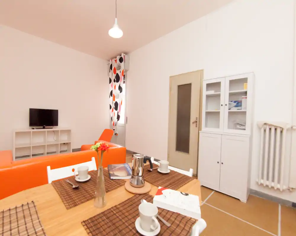 Espace de vie lumineux et moderne avec un canapé orange, une table dressée pour le café et une petite TV — idéal pour un séjour convivial.