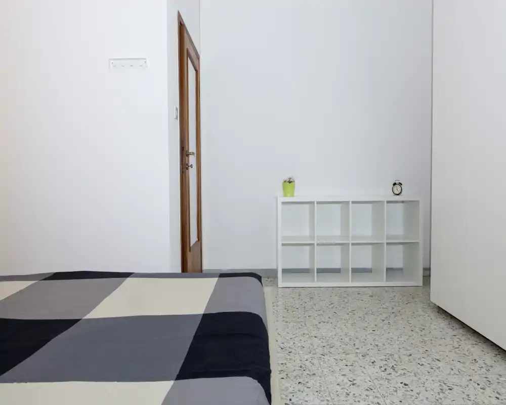 Camera da letto minimale e luminosa con letto basso e copriletto a quadri neutri, scaffale a cubi bianco e decorazioni semplici — ambiente luminoso e ordinato ideale per annunci.