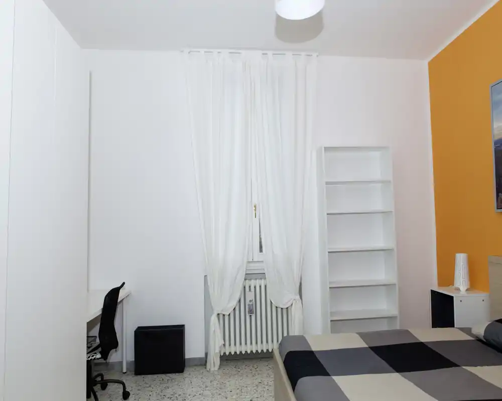 Camera da letto ordinata e moderna con letto matrimoniale, libreria e scrivania; luminosa e pulita con una parete arancione che dona calore.
