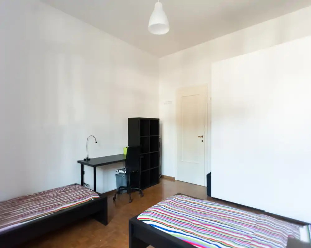 Bright, minimal bedroom with two single beds, a desk and shelving — ideal for students or shared stays. Clean lines, parquet floor and soft natural light create a calm, functional space.