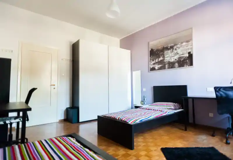 Bright, modern bedroom with a single bed, desk and wardrobe; colorful striped bedding and a framed city photo create a tidy, welcoming space ideal for a student or short-term stay.