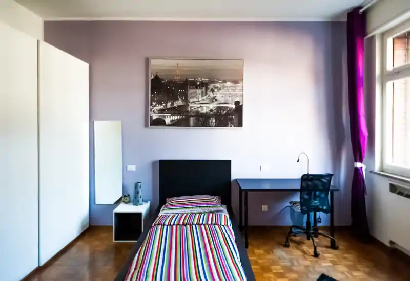 Bright, well-styled single bedroom with a striped bed, desk and wardrobe — ideal for a student or solo guest. Large window provides natural light and the simple modern decor creates a comfortable atmosphere.