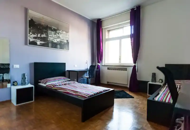 Well-lit twin bedroom with two single beds, striped bedding, a desk by the window and decorative wall art — ideal for students or shared rentals.