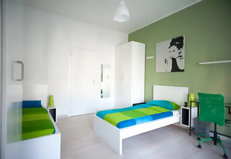 Bright, modern twin bedroom with two single beds, green-accented bedding and a coordinated workspace. Clean white furniture and lively wall art create a fresh, inviting atmosphere perfect for short-term rentals.