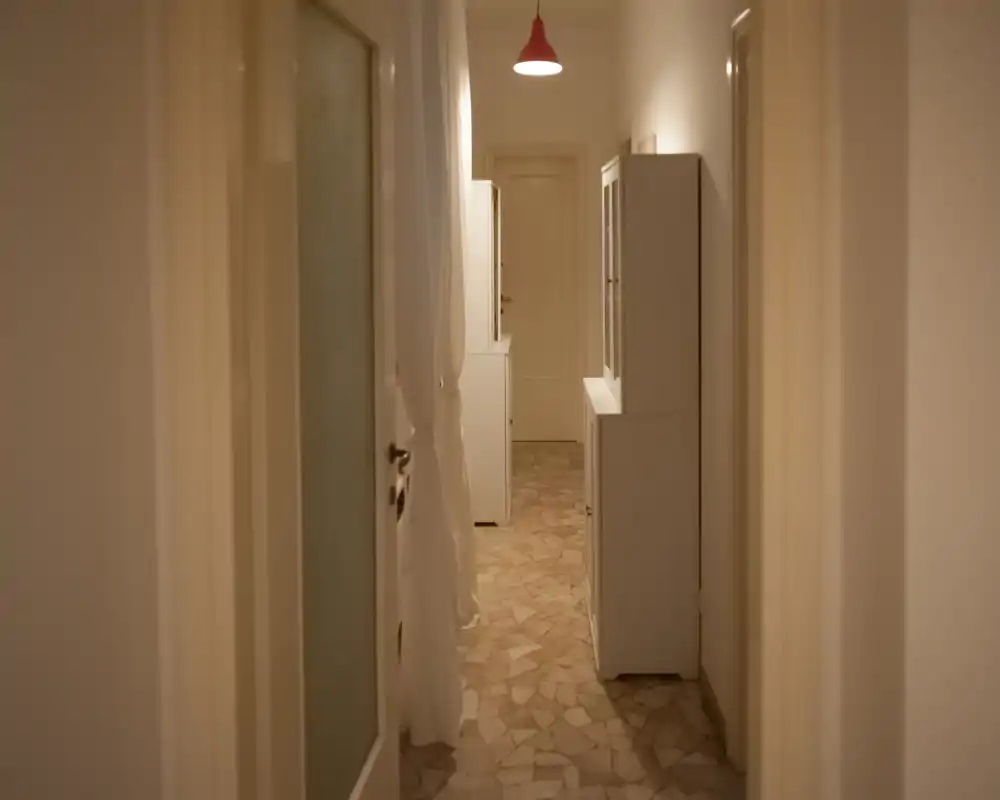 Narrow, well-kept hallway with tiled floor, neutral walls and built-in cabinets; warm overhead lighting creates a welcoming entry corridor.