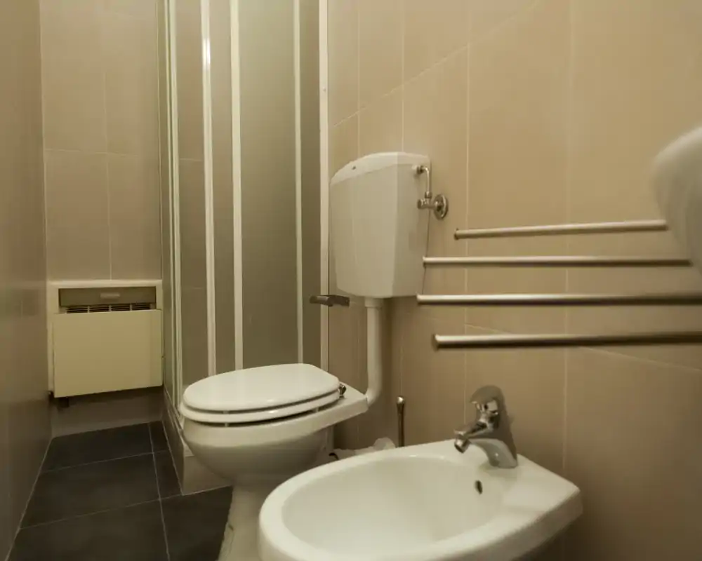 Compact, clean bathroom with a toilet, bidet and a shower enclosure; neutral tiles and chrome fixtures create a simple, functional space.