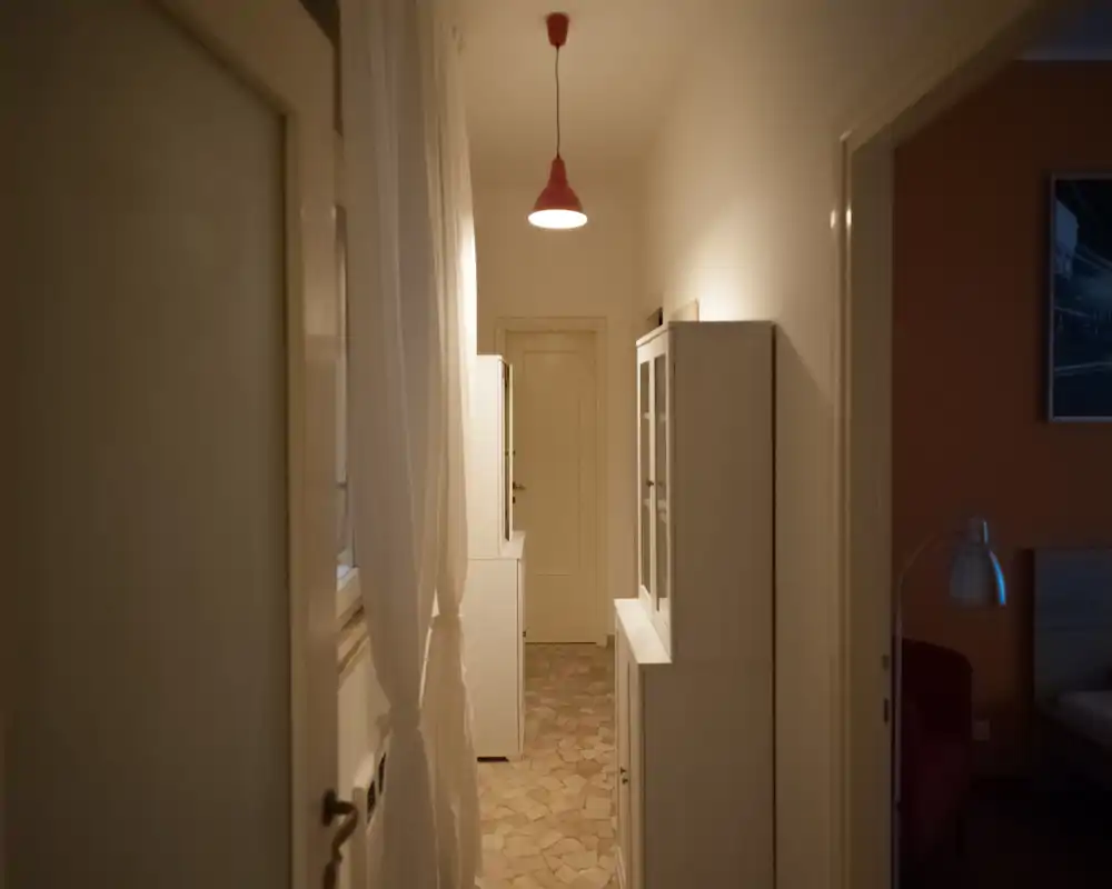 Narrow, well-kept hallway with tiled floor, white cabinets and a pendant lamp, leading to an interior door.