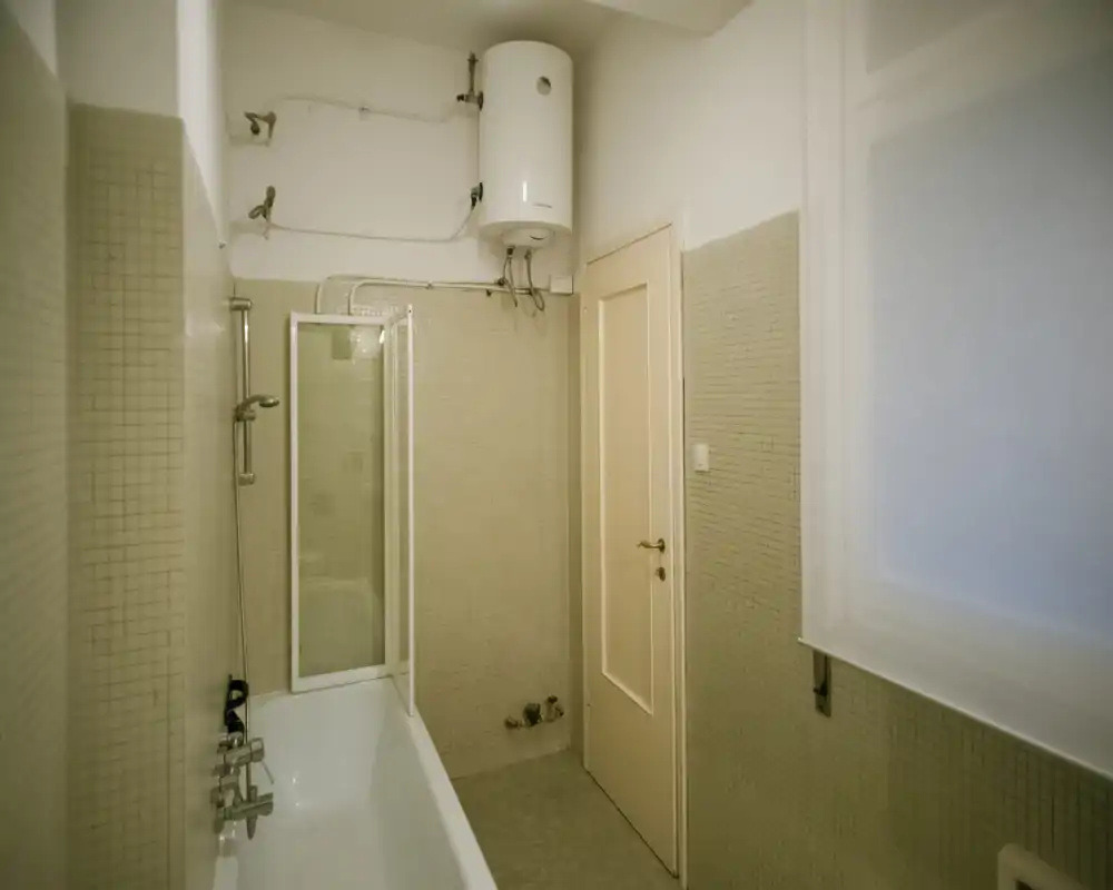 Bathroom with bathtub and overhead water heater, tiled walls and a shower screen; bright, functional layout suitable for rental listing photos.