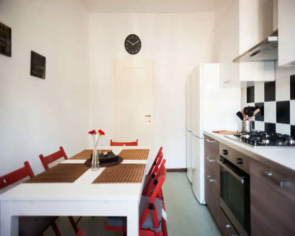 Bright combined kitchen and dining area with a white table set, red folding chairs, a fridge and a modern stove — ideal for compact apartment listings.