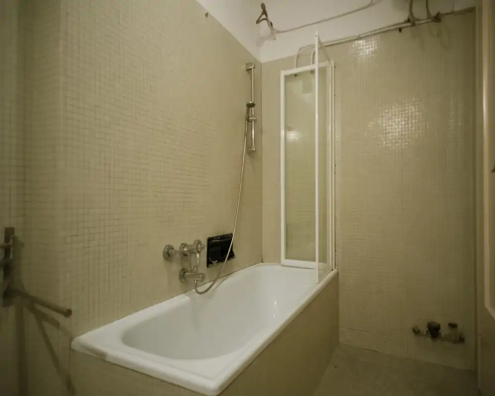 Bathroom with a built-in bathtub, wall-mounted shower head and tiled walls; compact layout suitable for a small apartment.