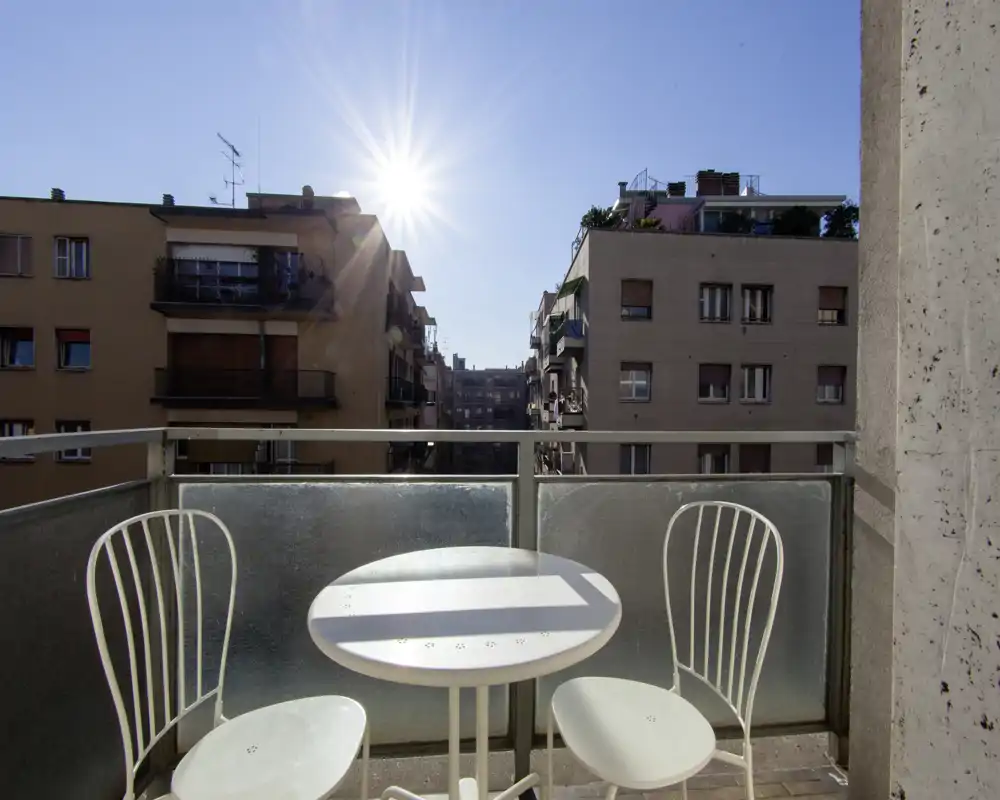 Balcone soleggiato con un piccolo tavolino rotondo e due sedie in metallo, con vista sugli edifici vicini — perfetto per il caffè mattutino.