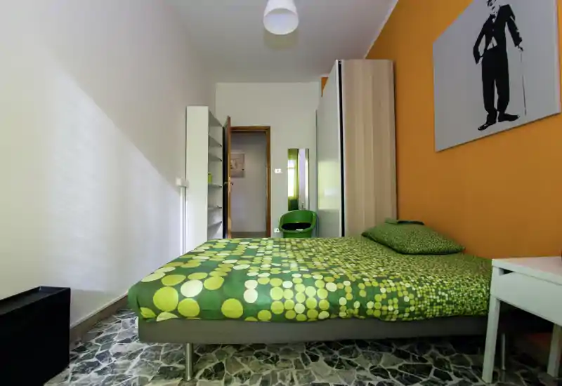 Camera da letto moderna e luminosa con letto matrimoniale verde a motivo, parete arancione e armadio — ambiente accogliente e ben illuminato, perfetto per annunci.