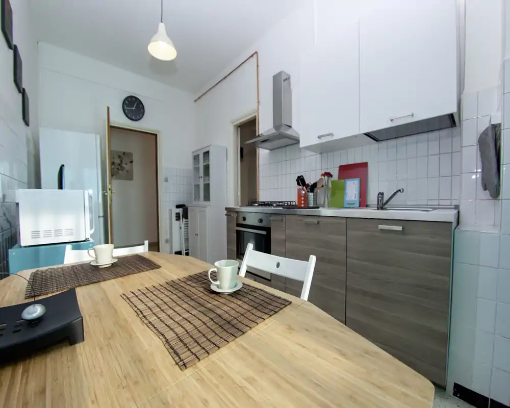 Cuisine lumineuse et fonctionnelle avec meubles bas modernes, cuisinière à gaz, évier et table en bois dressée avec sets et tasses — idéal pour repas décontractés.