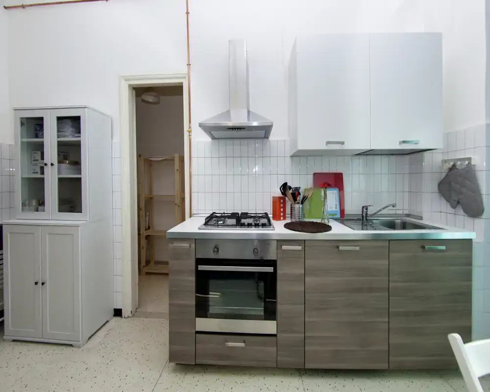 Cuisine compacte et moderne avec électroménagers en acier inoxydable, plaque à gaz et four intégré, placards hauts blancs et meubles bas effet bois ; propre, bien éclairée et prête à l'emploi.