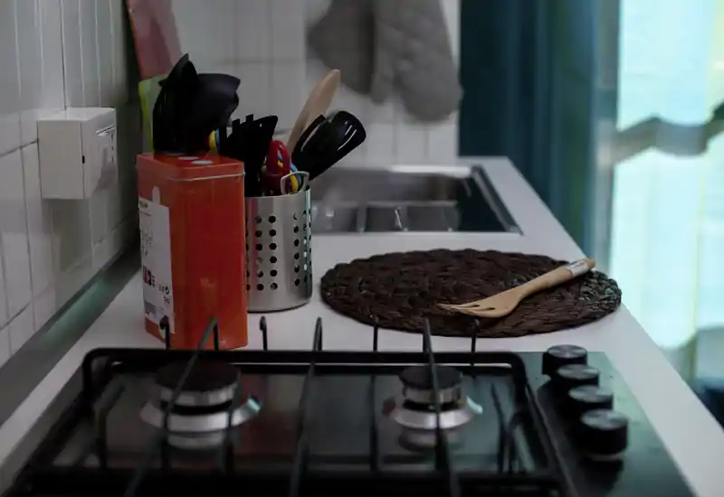 Bancone cucina compatto e curato con piano cottura a gas, porta utensili e lavello — ordinato e accogliente per preparare i pasti.