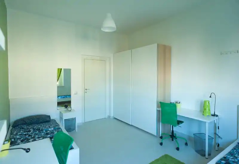 Camera da letto luminosa e moderna con letto singolo, scrivania e armadio; ambiente minimal e zona studio con sedia verde.