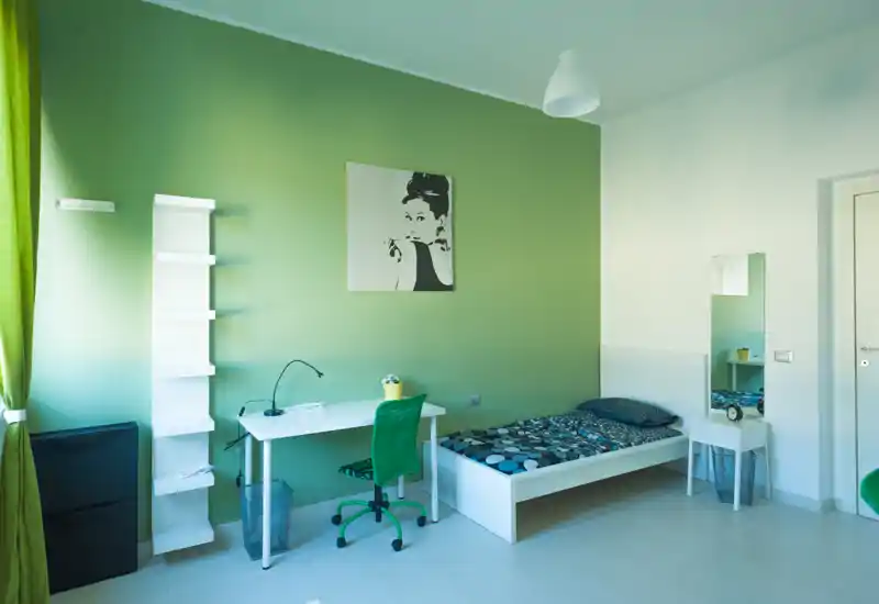 Camera singola luminosa e moderna con letto ordinato, scrivania e dettagli verdi che creano un'atmosfera fresca e rilassante.