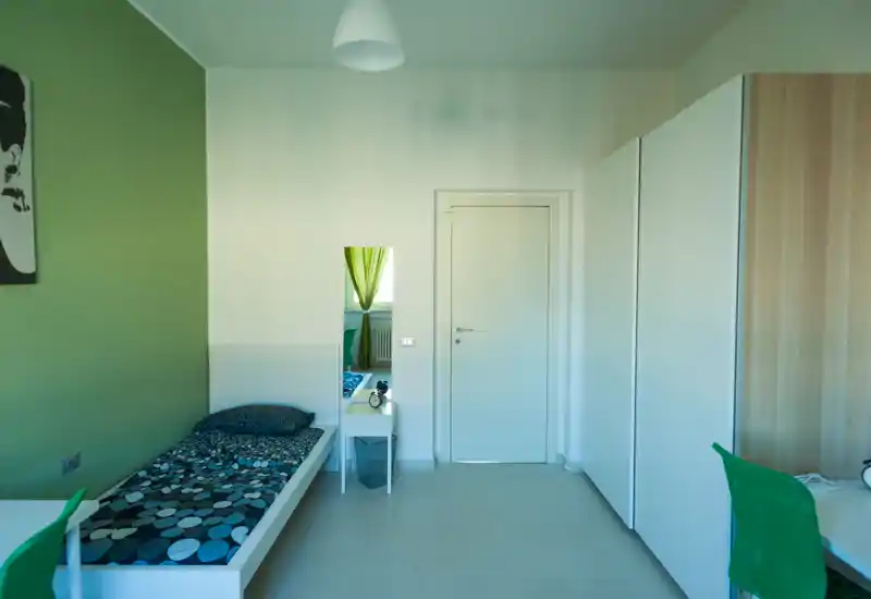 Camera singola moderna e luminosa con letto a una piazza, mobili bianchi e dettagli verdi che creano un ambiente tranquillo e curato.