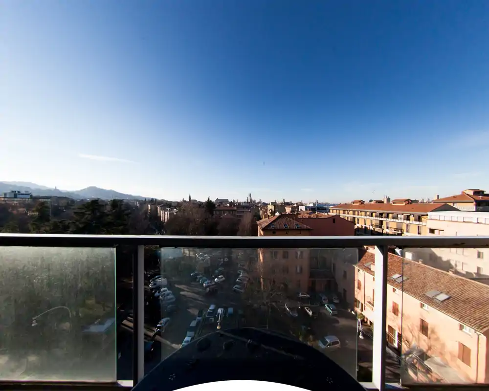 Bright balcony view overlooking city rooftops and distant hills, with a glass railing and open sky — ideal for morning coffee.