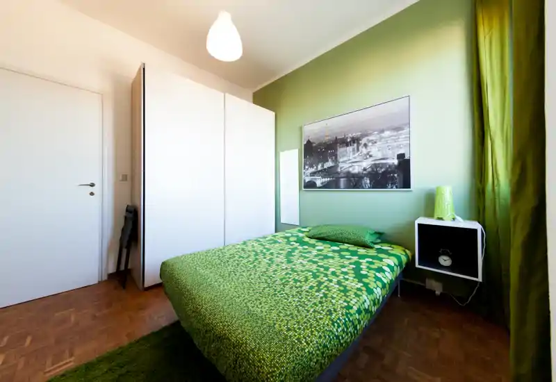 Camera da letto moderna e luminosa con tonalità verdi, letto matrimoniale con copriletto a fantasia, armadio e comodino — pulita, ben illuminata e di stile.