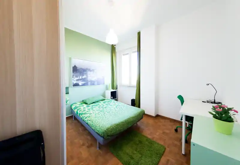 Camera da letto luminosa e ben arredata con letto a tema verde, tappeto e tende coordinati, scrivania vicino alla finestra e luce naturale che crea un'atmosfera fresca e accogliente.