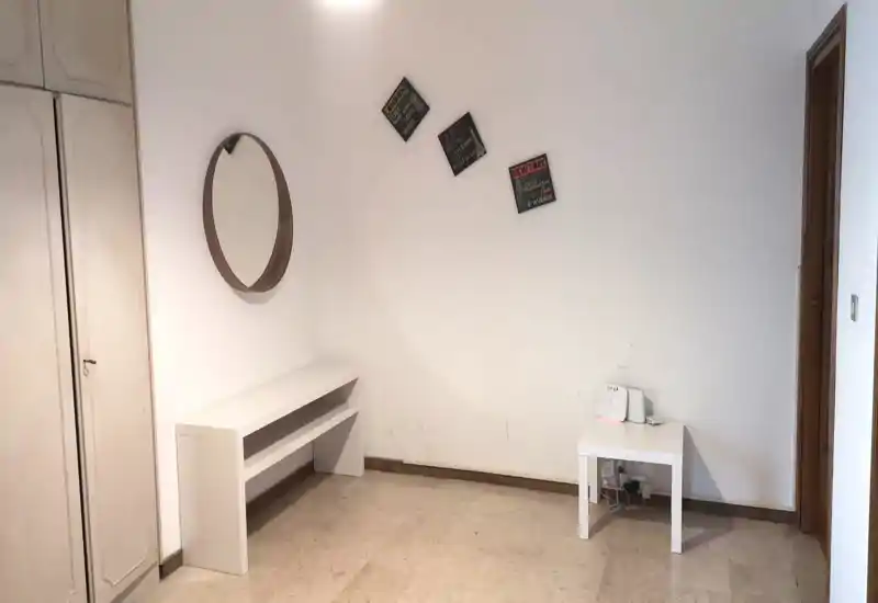 Pequeña entrada/pasillo con un banco, espejo de pared y mesa auxiliar. Paredes blancas y decoración mínima que crean un acceso limpio y sencillo.