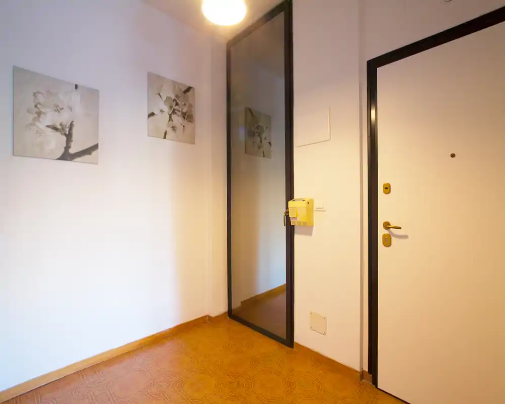 Vestíbulo luminoso y sencillo con un gran espejo en la pared, cuadros decorativos y una puerta de entrada segura — ideal para causar buena primera impresión.