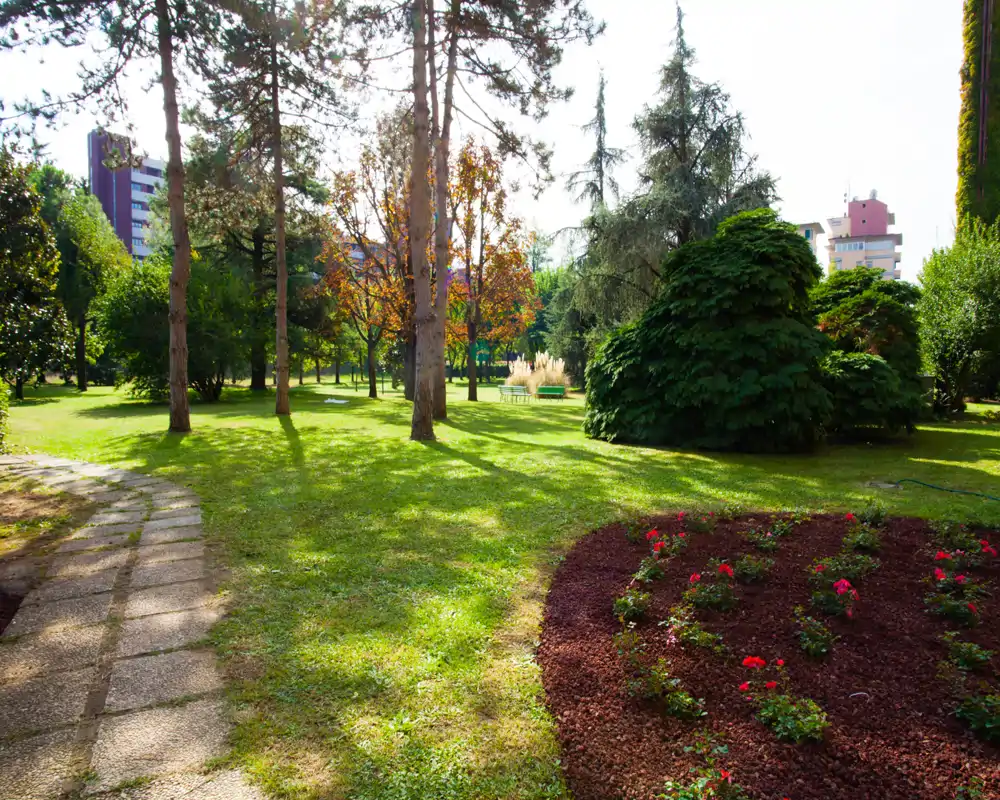 Jardín exterior luminoso y cuidado con césped, árboles y parterres de flores — ideal para paseos y relajación al aire libre.