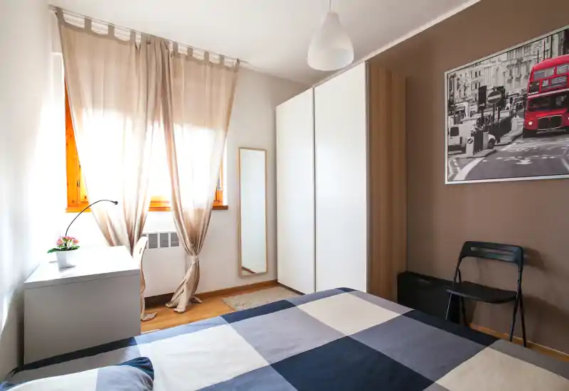 Bright, well-styled bedroom with a double bed, natural light from the window, a wardrobe and a small desk — ideal for a comfortable stay.