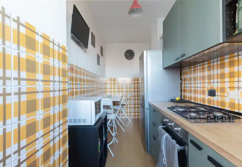 Cocina compacta y funcional con azulejos amarillos de diseño, placa de gas, frigorífico y una pequeña mesa — luminosa y ordenada, ideal para alquileres vacacionales.