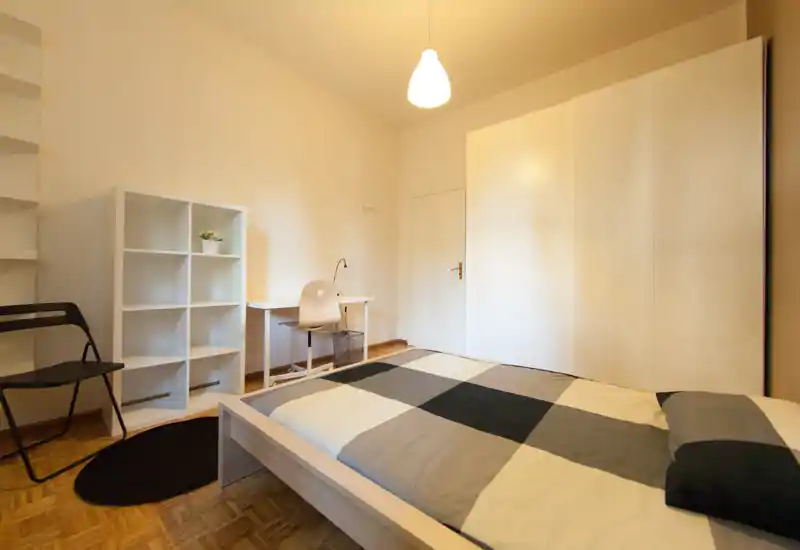 Bright, minimalist bedroom with a double bed, large wardrobe, desk and shelving — ideal for a comfortable single or couple stay.
