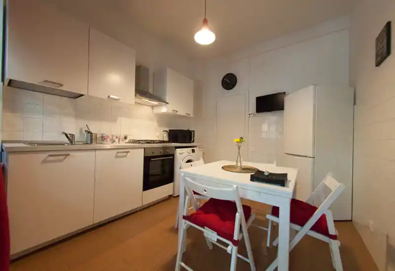 Bright, compact kitchen with white cabinetry, built-in oven and a small dining table with cushioned chairs — ideal for cozy meals and efficient cooking.