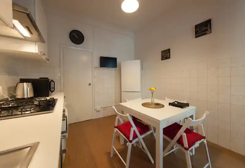 Compact, tidy kitchen with a gas hob, microwave and refrigerator, plus a small dining table with cushioned folding chairs — well suited for a cozy apartment stay.