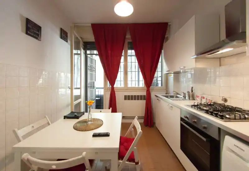 Bright, compact kitchen with a gas hob, oven and a small dining table. Red curtains and cushions add a cozy touch and the layout maximizes the available space.