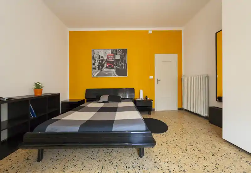 Camera da letto luminosa e moderna con letto matrimoniale centrato su una parete arancione, comodini e contenitori minimal — linee pulite e colore deciso rendono l'ambiente accogliente.