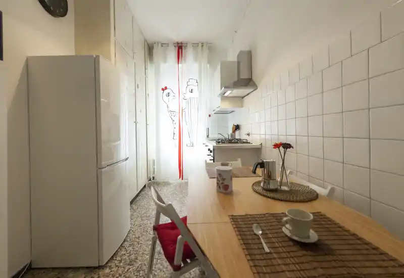 Cucina compatta e luminosa con tavolo in legno, piano cottura a gas, frigorifero e tocchi decorativi vivaci — perfetta per pasti accoglienti in un piccolo appartamento.