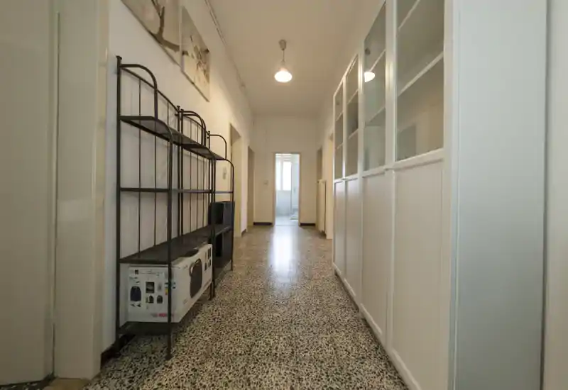 Lungo corridoio/ingresso ben illuminato con pavimento in graniglia, scaffalature a sinistra e armadi a parete a destra — ideale come corridoio d'ingresso organizzato.